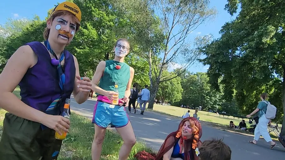 Drei Clowns mit Getränken in sonnigem Park.