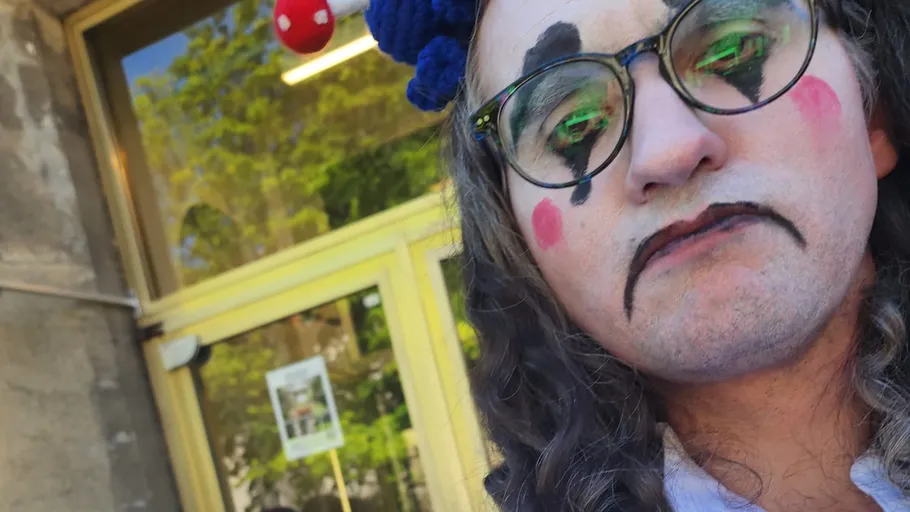 Person with clown makeup outside building entrance.