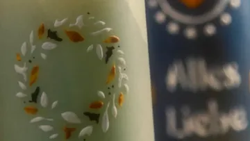 Grüne Kerze mit Blattdesign neben blauer Kerze.