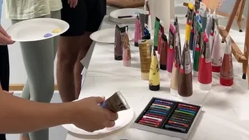 People holding plates near art supplies table.