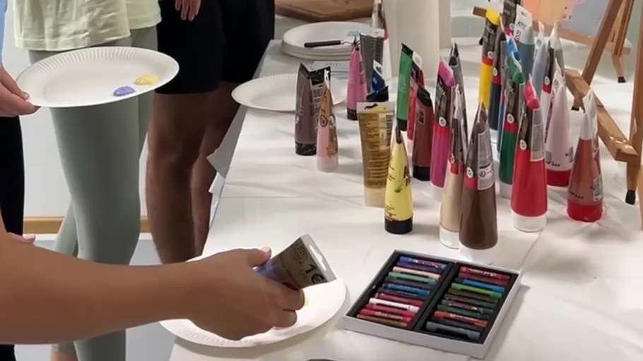 People holding plates near art supplies table.
