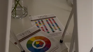 Color charts on a desk beside a vase.