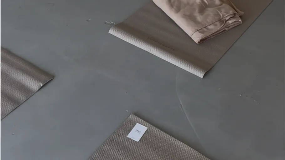 Yogamatten auf grauem Boden mit gefaltetem Handtuch.