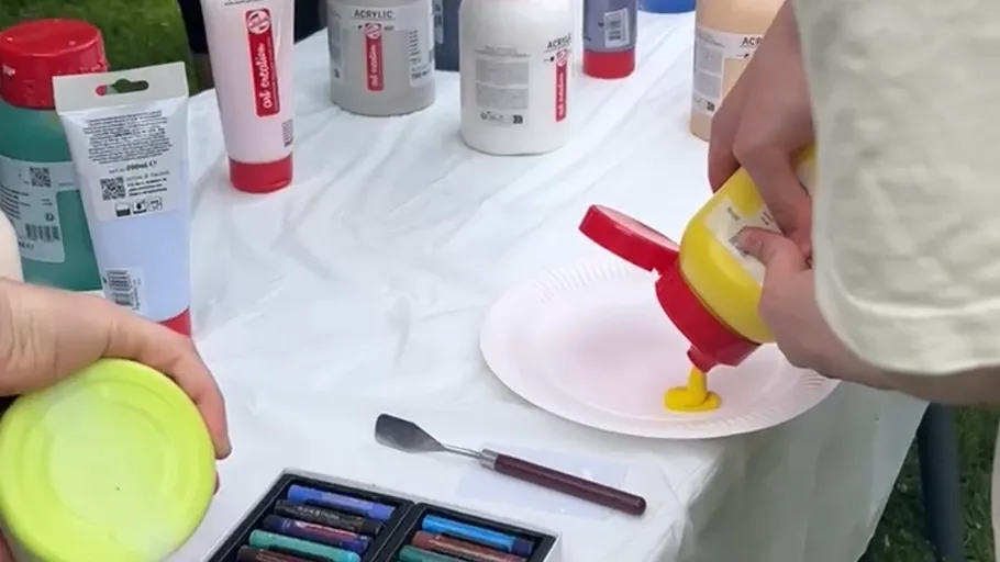 Person pours yellow paint onto paper plate.