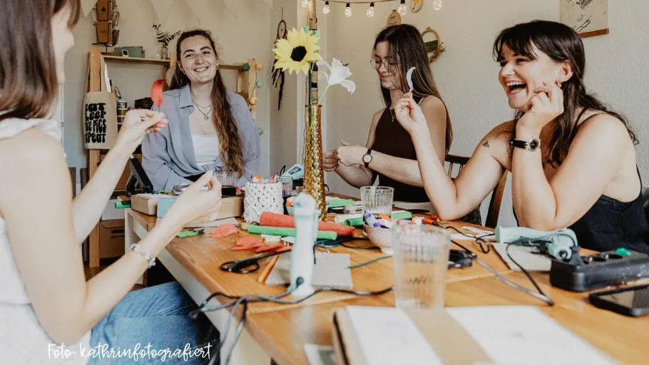 Frauen basteln mit Blumen am Tisch, lächelnd.