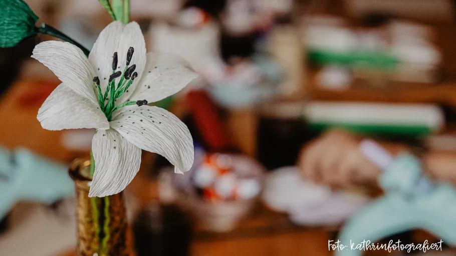 Weiße Blume mit Bastelwerkzeugen im Hintergrund.