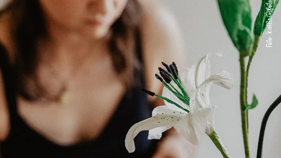 Weiße Blume im Vordergrund, unscharfe Person im Hintergrund.