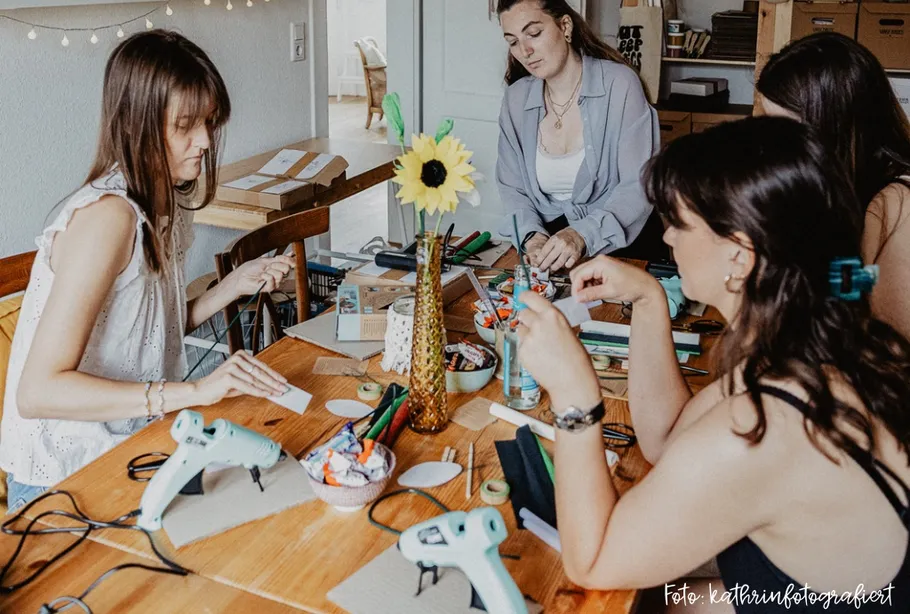 Women crafting with tools on wooden table.
