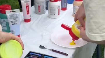 Hände gießen gelbe Farbe auf Pappteller.
