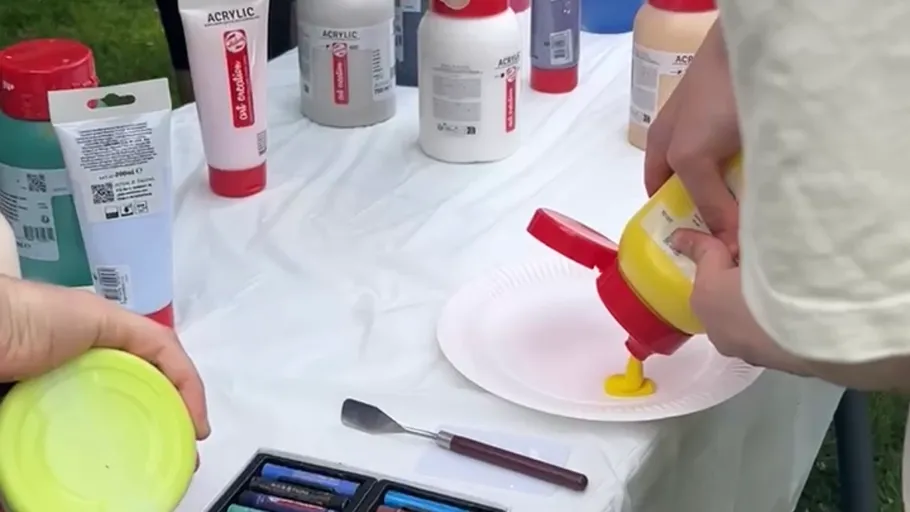 Hände gießen gelbe Farbe auf Pappteller.