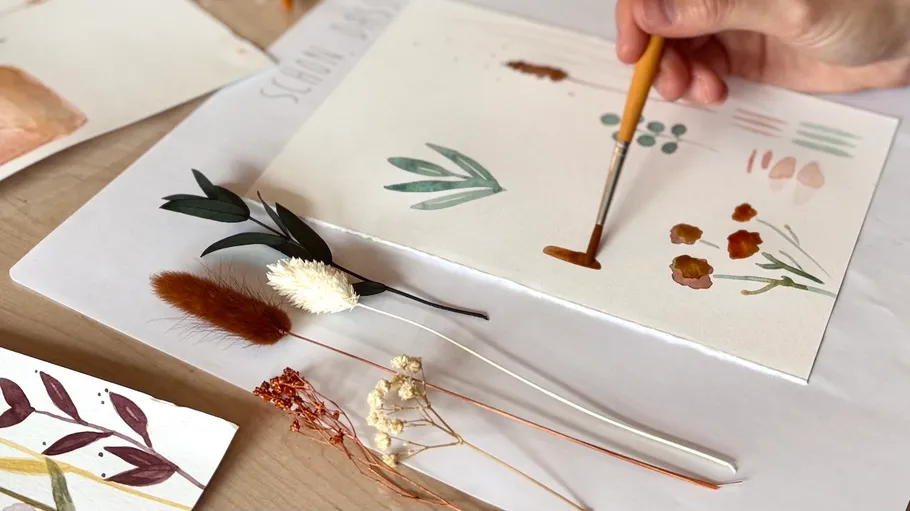 Hand paints leaves and flowers on paper.