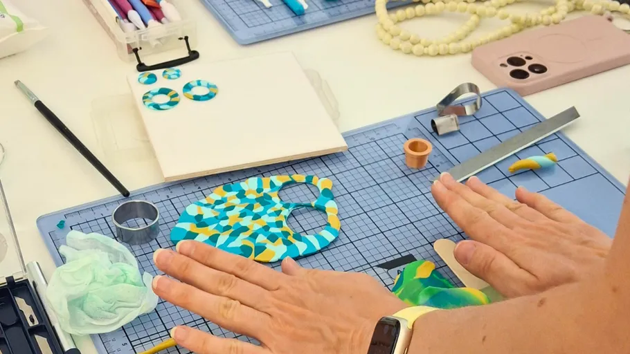 Hands crafting earrings on a cutting mat.