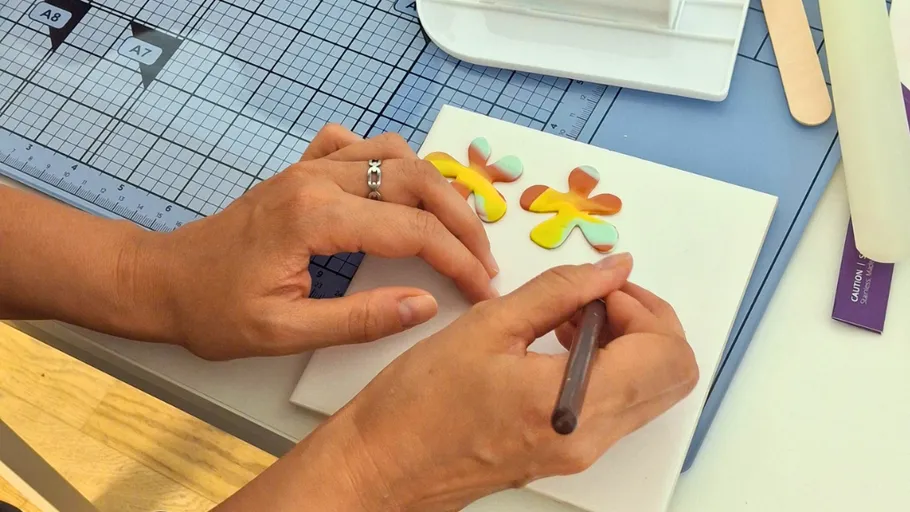 Hands crafting with colorful clay flowers.