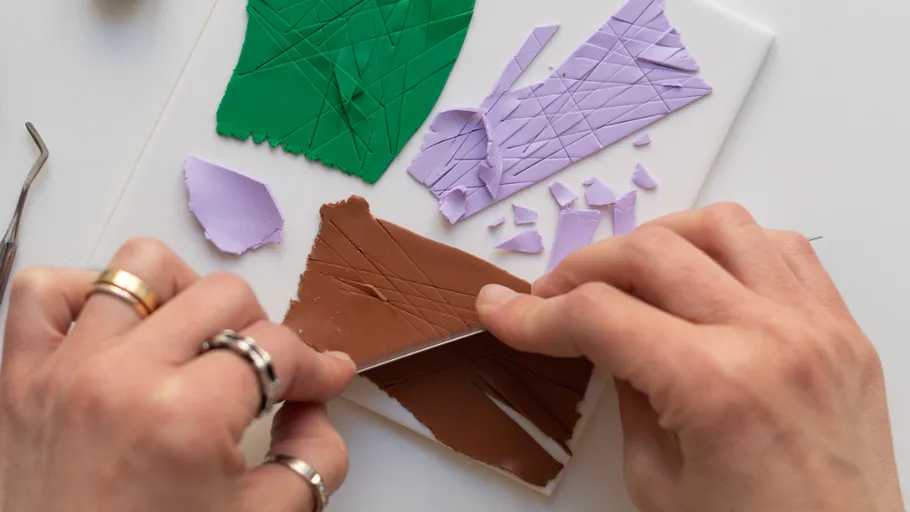 Hands cutting colored clay shapes on table.