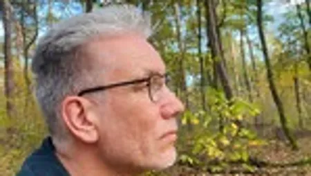 Mann mit Brille im Wald von der Seite.