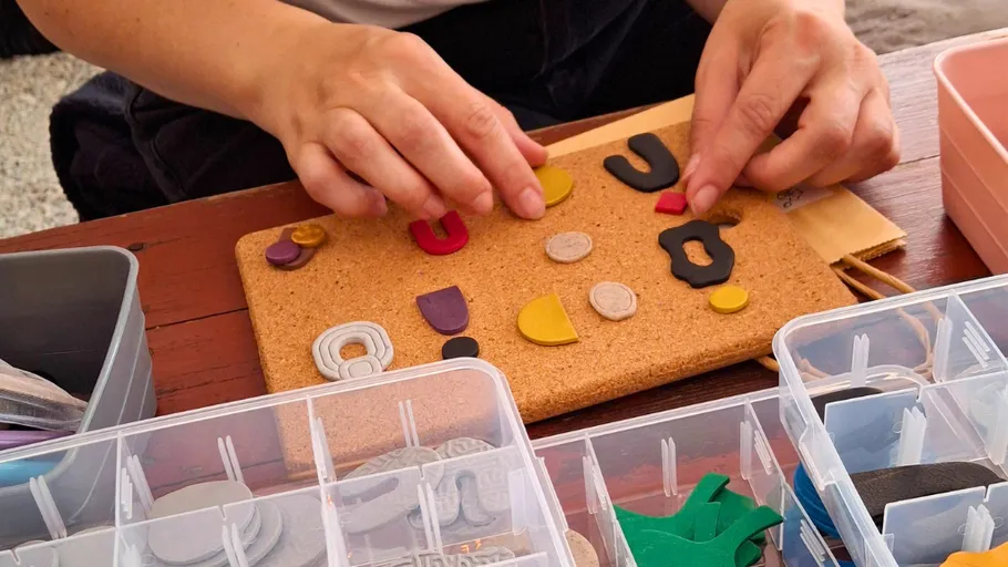 Hands arranging craft materials on corkboard.