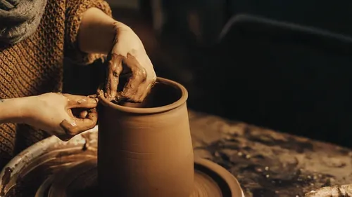Person shaping clay pot on pottery wheel.