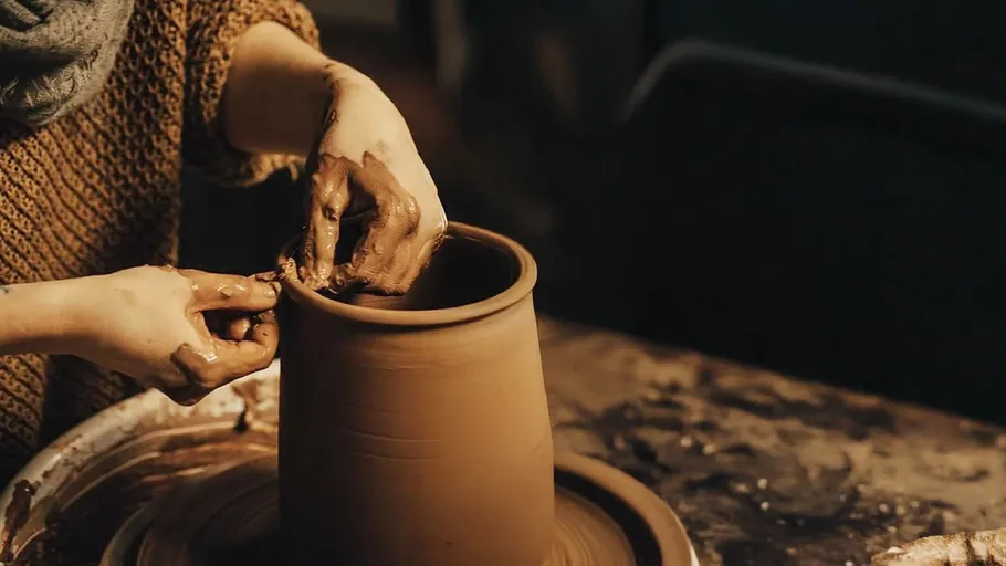 Person shaping clay pot on pottery wheel.