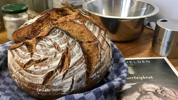Frisches Brot auf Tuch, Küchengeräte dahinter.