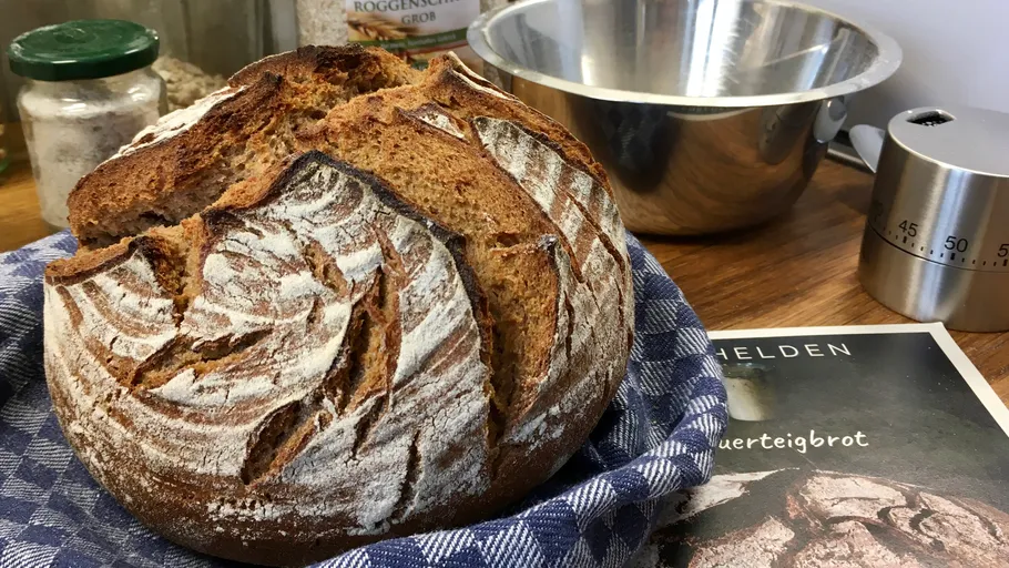 Frisches Brot auf Tuch, Küchengeräte dahinter.