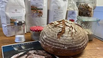 Loaf of sourdough bread with flour and jars.