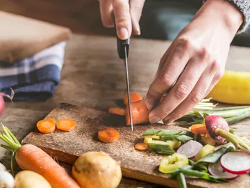 A hand cuts carrots on a wooden board.