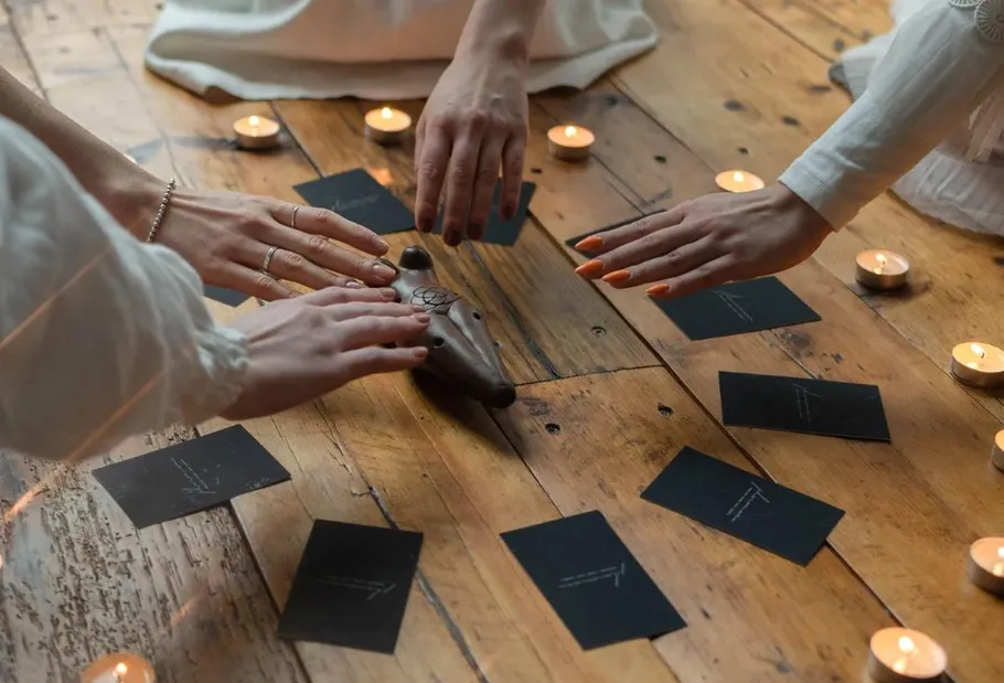 Hands touching object surrounded by candles and cards.