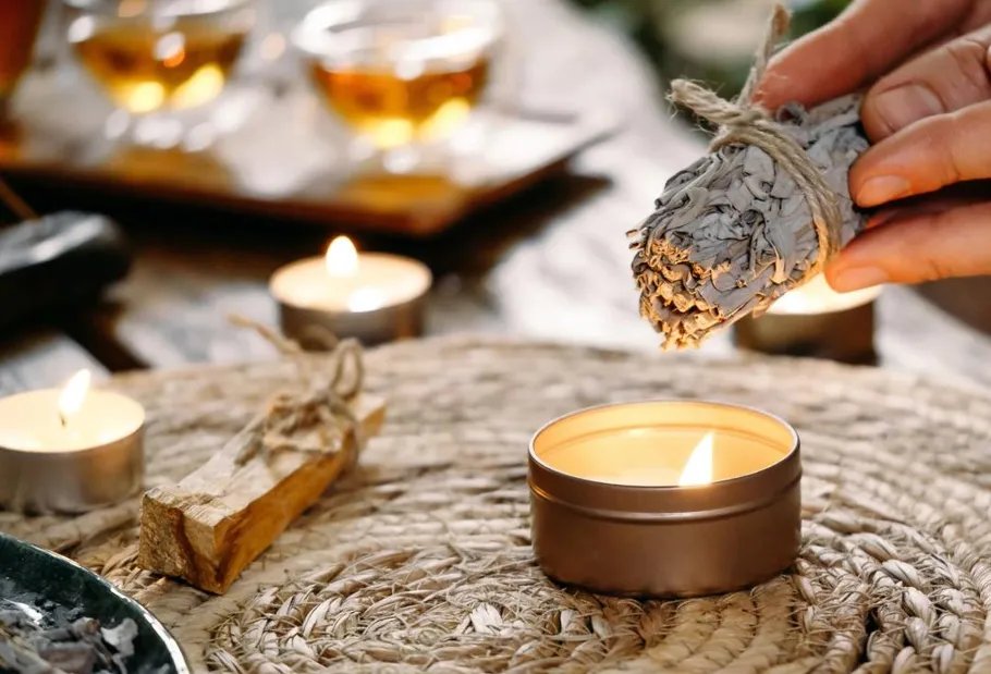 Hand holds sage over candle on woven mat.