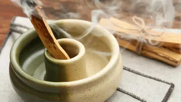 Burning palo santo in ceramic holder, smoke rising.