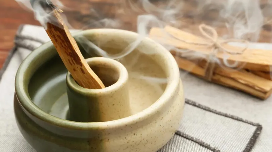 Burning palo santo in ceramic holder, smoke rising.
