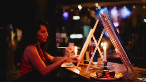 Woman painting at candlelit table in dark room.