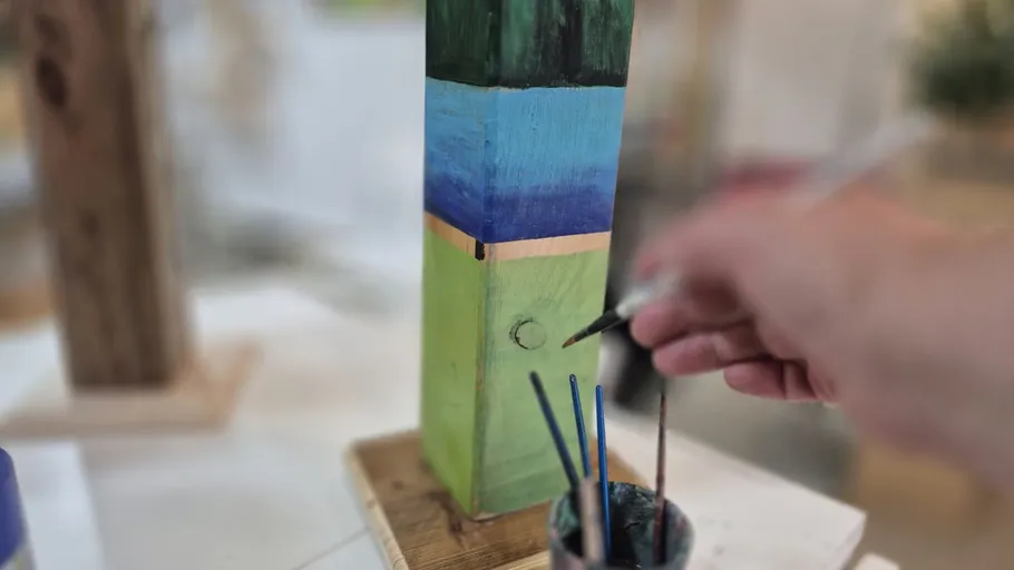 Person painting colorful wooden sculpture indoors.