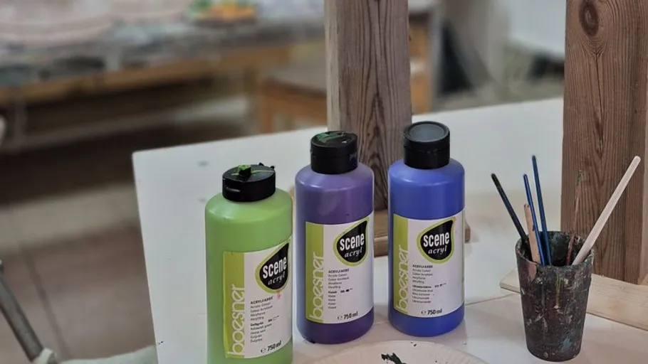 Three paint bottles next to paintbrushes on table.