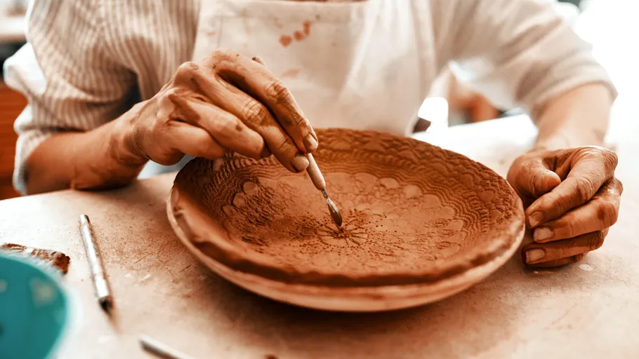 Person carving design into clay bowl.