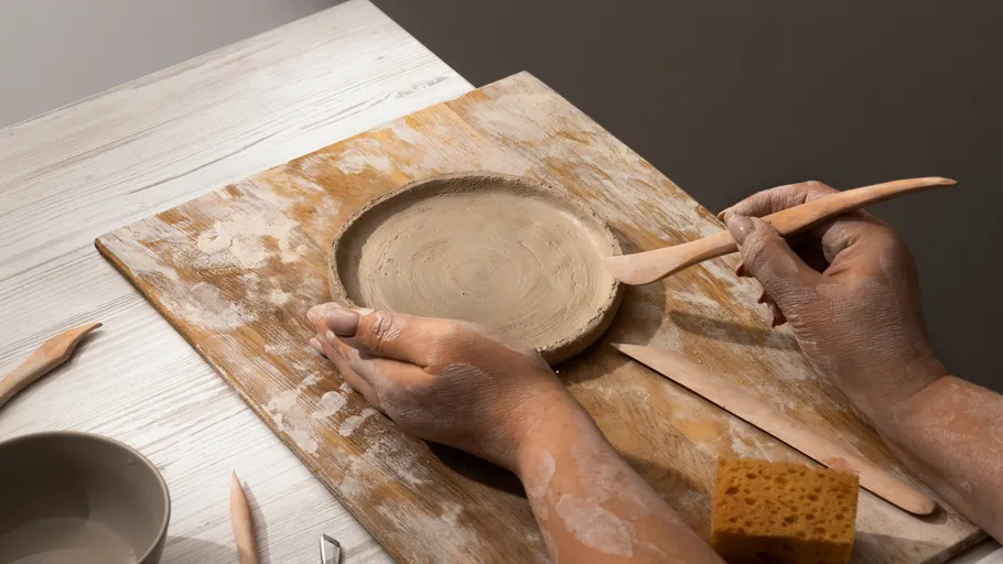 Hands shaping clay on wooden board.