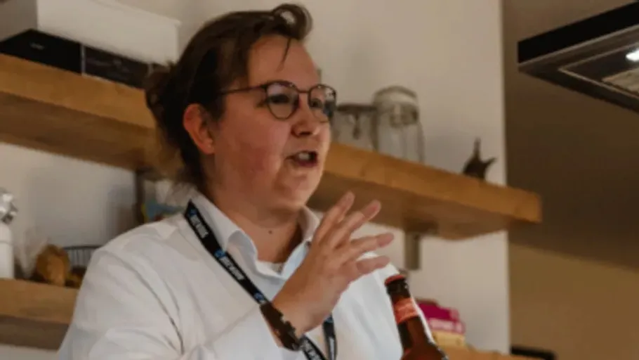 Person talking, holding a beer bottle, indoors.