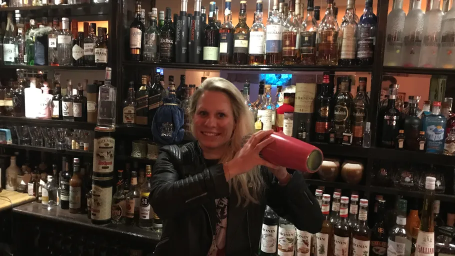 Woman shaking cocktail shaker in bar.