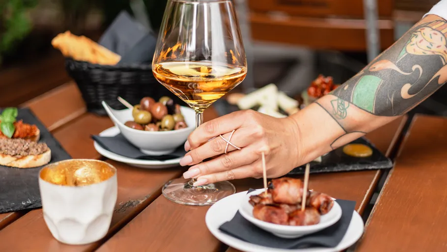 Tätowierte Hand hält Weinglas, verschiedene Snacks.
