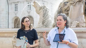 Two women talking near a fountain sculpture.