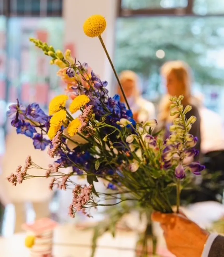 Hand holding a colorful flower bouquet indoors.