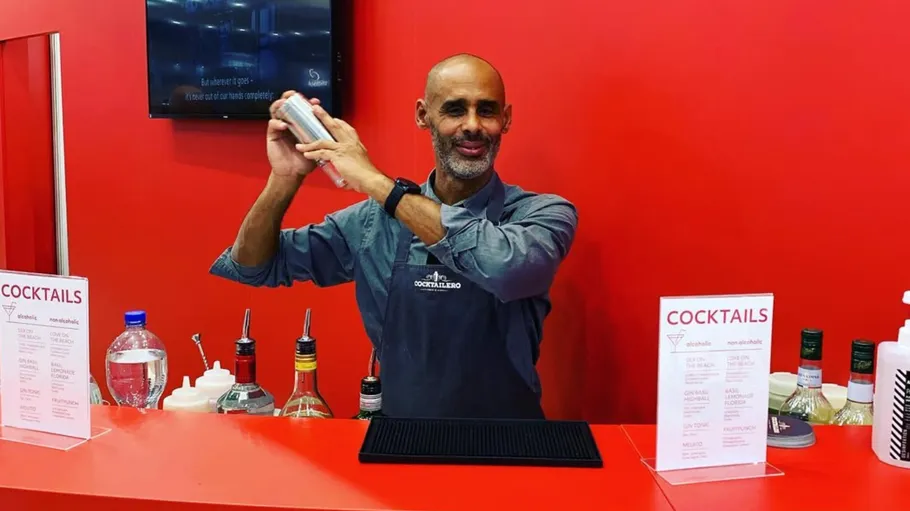 Bartender shaking cocktail behind red counter.