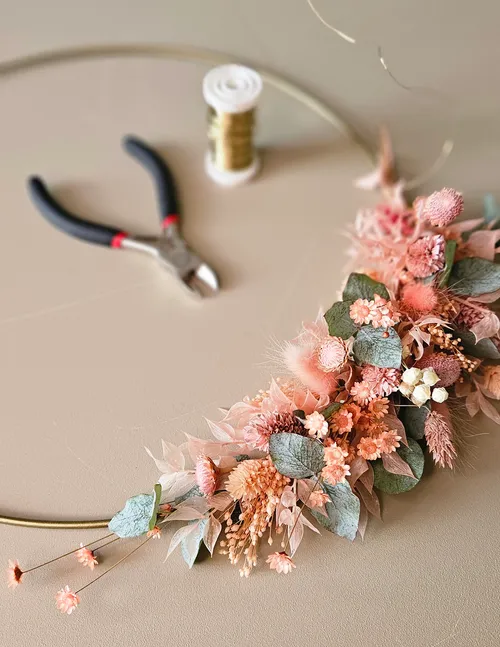 Floral arrangement on wire hoop with tools nearby.