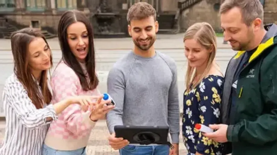 Fünfergruppe schaut draußen auf ein Tablet.