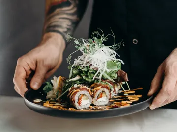 Ein Mensch hält einen Teller mit Sushi und Salat.