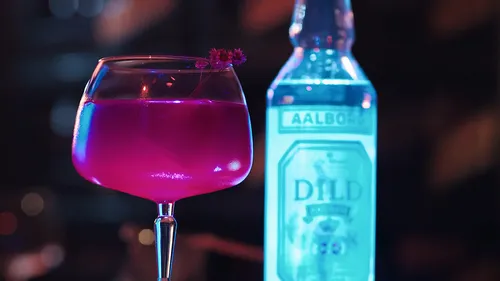 Pink cocktail next to a glowing bottle.