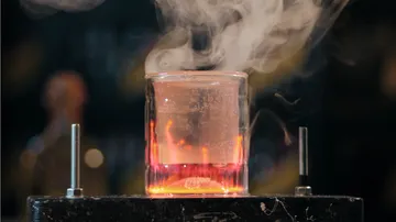 Glass beaker emitting steam on dark background.