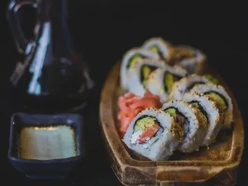 Sushi auf einem Holzbrett, umgeben von Sojasauce und Ingwer.