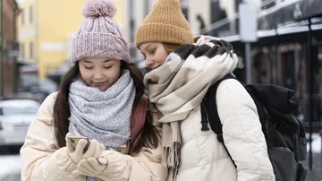 Zwei Personen in Winterkleidung sehen auf Smartphone.
