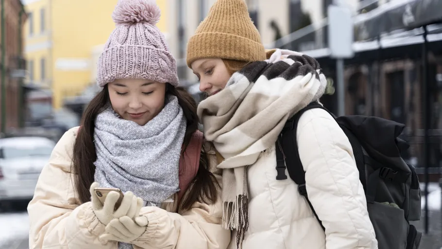 Two people in winter clothing look at smartphone.