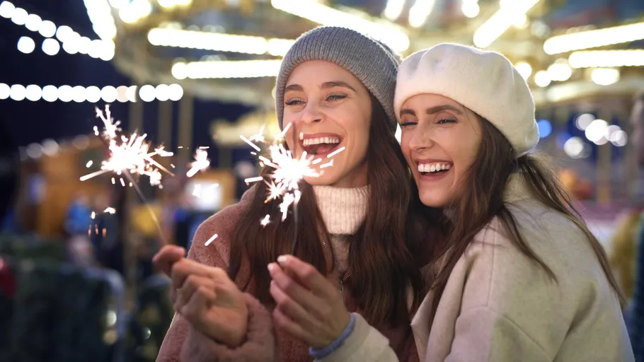 Two women holding sparklers, smiling at night.